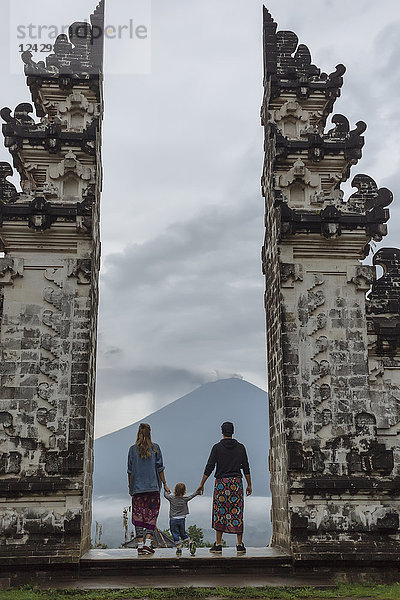 Rückansicht einer Familie  die am alten Pura Lempuyang-Tempel steht und auf den Vulkan Mount Agung blickt  Bali  Indonesien