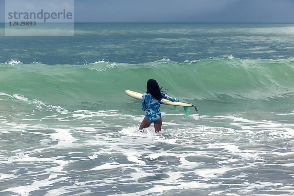 Rückansicht einer Frau mit Surfbrett im Meer