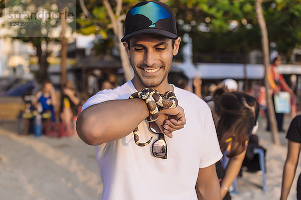 Aufnahme eines lächelnden Mannes mit Baseballmütze  der eine exotische Schlange in der Hand hält  Kuta  Bali  Indonesien