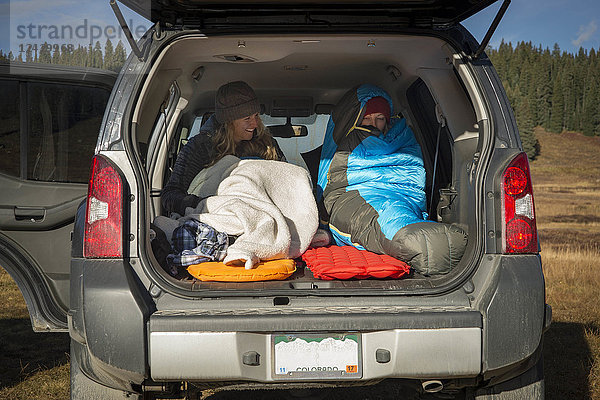 Zwei junge Frauen in Schlafsäcken wachen auf  nachdem sie im Kofferraum eines Autos geschlafen haben  Crested Butte  Colorado  USA