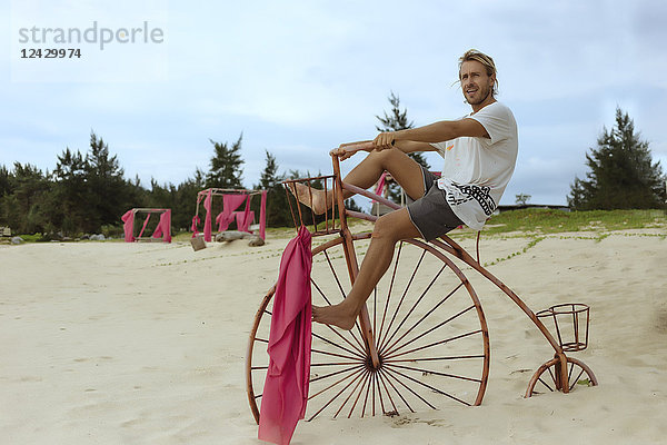 Totale Aufnahme eines jungen Mannes  der auf einem hölzernen  dekorativen Penny-Farthing-Fahrrad am Strand sitzt  Banda Aceh  Sumatra  Indonesien