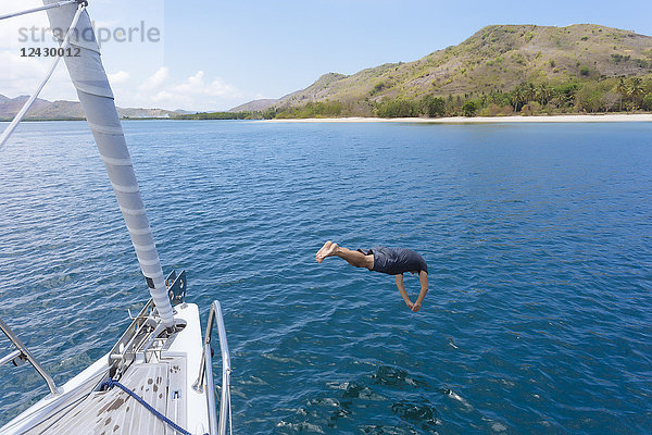 Totale Aufnahme eines Mannes in der Luft  der vom Boot aus ins Wasser taucht  Lombok  Indonesien