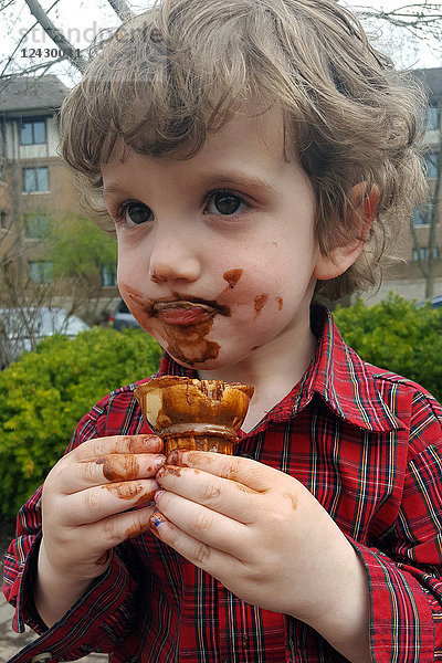Junge mit schmutzigem Gesicht nach dem Verzehr von Schokoladeneis im Freien