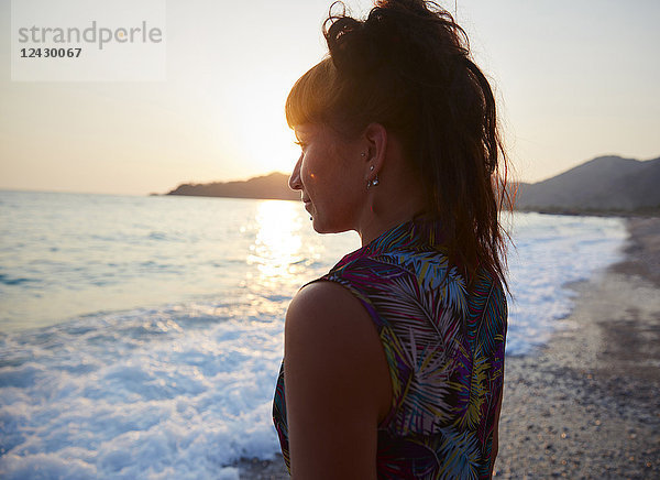Kopf und Schultern Porträt der schönen jungen Frau am Strand bei Sonnenuntergang