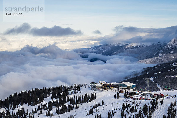 Whistler Blackcomb Ski Resorts Roundhouse und Peak 2 Peak Gondola sitzen an einem sonnigen Tag auf dem Gipfel des Berges  während im Tal darunter schwere Wolken aufziehen  Whistler  British Columbia  Kanada