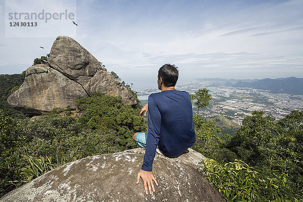 Rückansicht eines einzelnen Mannes  der auf einem Felsen in natürlicher Umgebung sitzt  Tijuca Forest  Rio de Janeiro  Brasilien