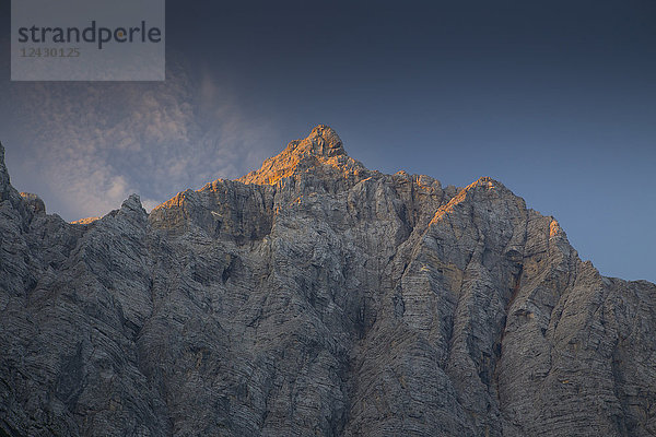 Die steile Nordwand des Triglav in Slowenien wird von der aufgehenden Sonne orange gefärbt. Dieser Berg ist ein legendärer Gipfel des Landes  und die Nordwand ist eine große Herausforderung für erfahrene Kletterer. Das Bild wurde vom Vrata-Tal aus aufgenommen.