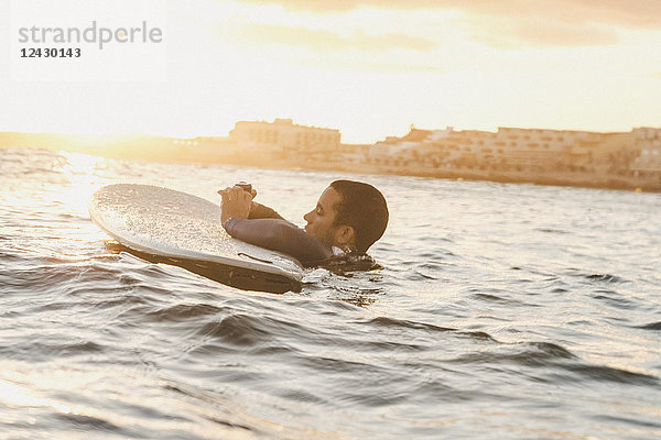 Seitenansicht eines Surfers  der eine tragbare Kamera im Meer überprüft