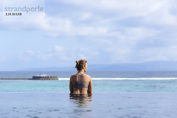 Rückansicht einer jungen Frau im Badeanzug im Schwimmbad mit Blick auf das Meer