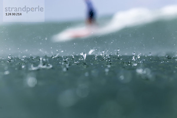Close up Schuss von Regentropfen im Meer und Surfer im Hintergrund