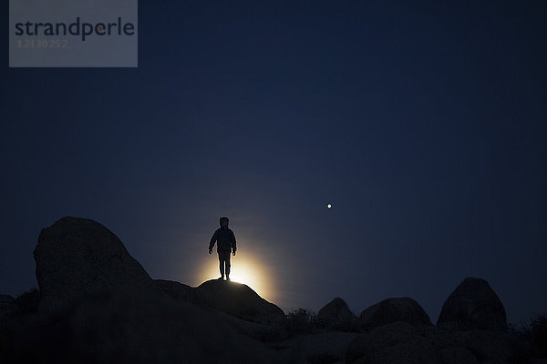 Silhouette eines Jungen auf einer Felsformation bei Nacht