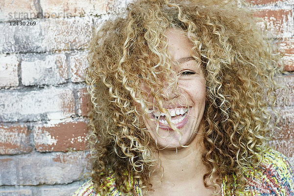 Porträt einer jungen lächelnden Frau mit langen lockigen blonden Haaren  die in die Kamera schaut.