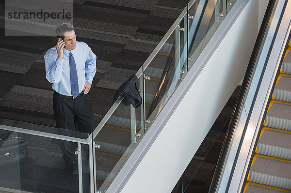 Blick von oben auf einen Geschäftsmann  der sein Telefon in der Lobby eines Konferenzzentrums benutzt.