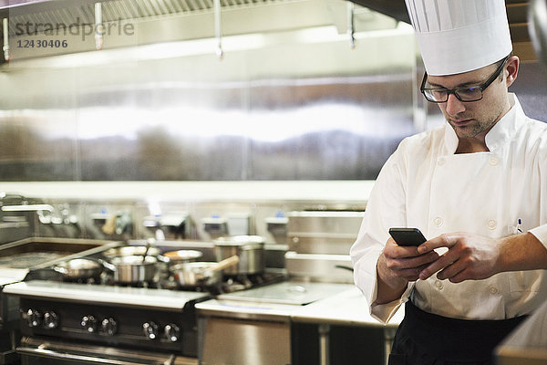 Ein kaukasischer Koch überprüft sein Mobiltelefon in einer Großküche