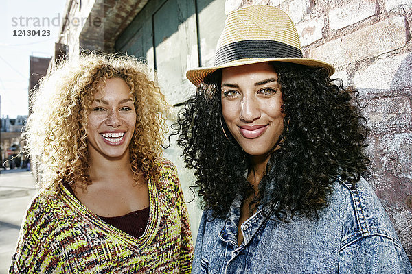 Porträt von zwei lächelnden jungen Frauen mit langen lockigen schwarzen und blonden Haaren  die in die Kamera schauen.