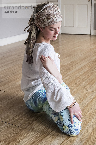 Junge Frau mit Kopftuch und weißer Bluse sitzt in Yoga-Pose auf dem Boden.