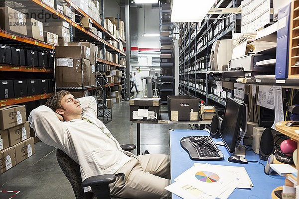 Ein männlicher Techniker  der sich an seinem Schreibtisch in der Ersatzteilabteilung eines technischen Forschungs- und Entwicklungsstandorts ausruht.