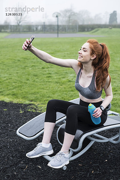 Lächelnde junge Frau mit langen roten Haaren in Sportausrüstung  die im Freien Sport treibt.