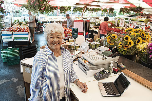 Ältere Frau steht an der Kasse eines Lebensmittel- und Gemüsemarktes und lächelt in die Kamera.