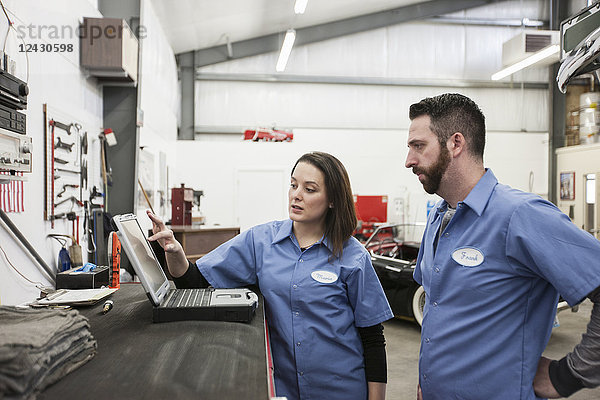 Zwei Mechaniker arbeiten an einem Laptop-Computer in einer Reparaturwerkstatt.