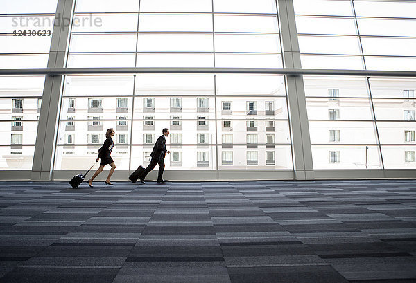 Männliche und weibliche Geschäftsleute rennen an einem Fenster in der Lobby eines Konferenzzentrums vorbei