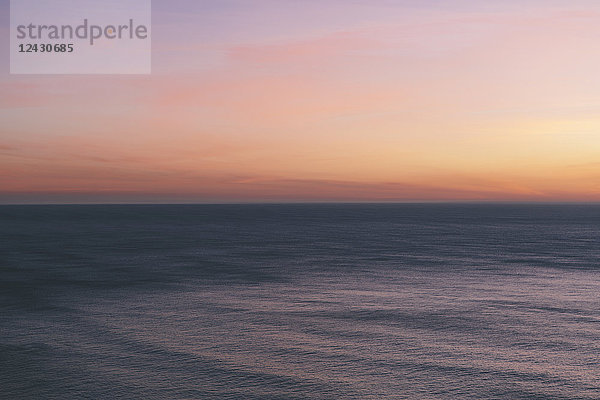 Blick aufs Meer über den Ozean in der Abenddämmerung  das Licht des Sonnenuntergangs am Horizont und die ruhige  wellige Meeresoberfläche.