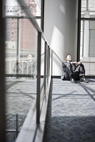 Blick von unten auf einen kaukasischen Geschäftsmann  der am Fuß einer Säule in einem Kongresszentrum eine Pause einlegt.