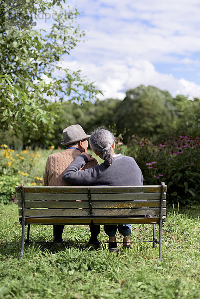 Ehemann und Ehefrau  Rückansicht eines älteren Mannes mit Hut und einer Frau  die Seite an Seite auf einer Bank in einem Garten sitzen.