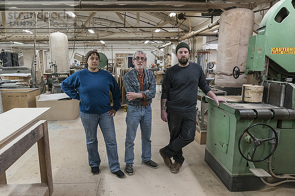 Portrait eines Teams von drei gemischtrassigen Tischlern in einer großen holzverarbeitenden Fabrik.
