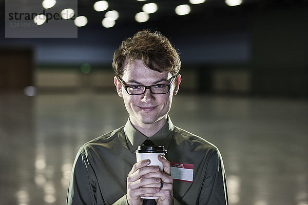 Ein junger  hipper Geschäftsmann  der in einem schwach beleuchteten und dunklen Ausstellungsbereich in einem Kongresszentrum steht.