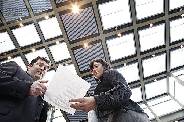Zwei Geschäftsleute gehen in der Lobby eines großen Kongresszentrums den Papierkram durch.