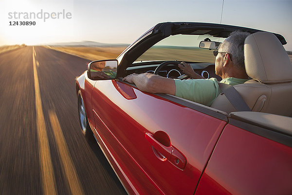 Ein älterer hispanischer Mann am Steuer seines Cabrio-Sportwagens bei Sonnenuntergang im Osten des Staates Washington  USA.