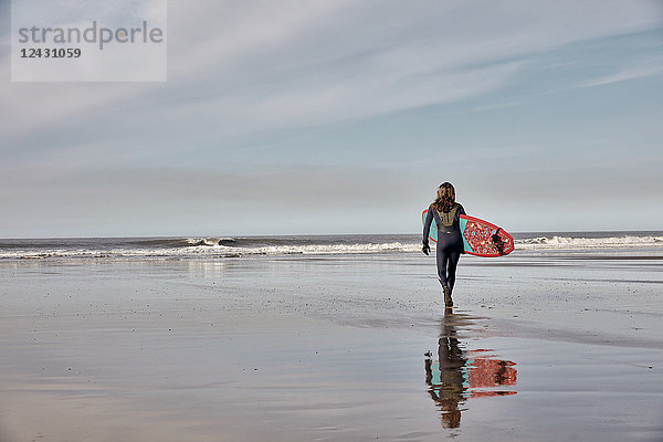 Mann mit einem Surfbrett in der Hand  der bei Ebbe auf das Meer hinausgeht.