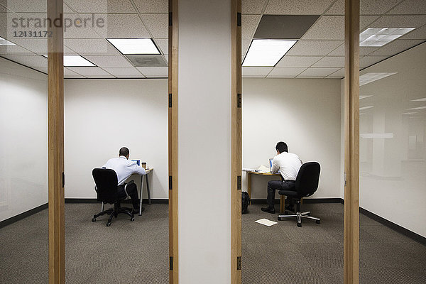 Ein Blick auf zwei Geschäftsleute  die auf gegenüberliegenden Seiten einer Wand in zwei verschiedenen Büroräumen arbeiten.