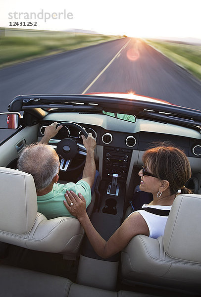 Ein Blick von hinten auf ein älteres Ehepaar in einem Cabrio-Sportwagen  das bei Sonnenuntergang im Osten des Bundesstaates Washington  USA  auf einer Autobahn fährt.