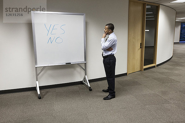 Ein schwarzer Geschäftsmann  der nachdenkt und vor einem Büro-White-Board steht  auf dem die Worte Ja und Nein geschrieben stehen.