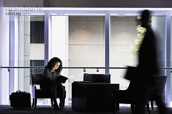 Eine schwarze Geschäftsfrau sitzt vor den Fenstern in einem abgedunkelten Lobbybereich eines Kongresszentrums.