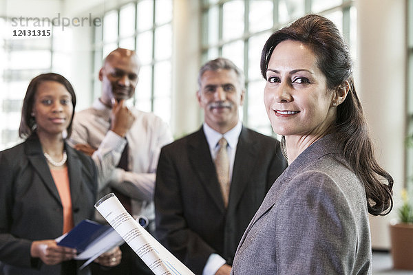 Ein gemischtrassiges Gruppenporträt von Geschäftsleuten  die in der Lobby eines Kongresszentrums stehen  mit einer Geschäftsfrau an der Spitze.