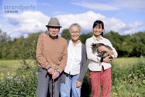 Lächelnde Frau hält eine graue Katze  die im Freien steht  mit einem älteren Mann und einer älteren Frau  die in die Kamera lächeln.
