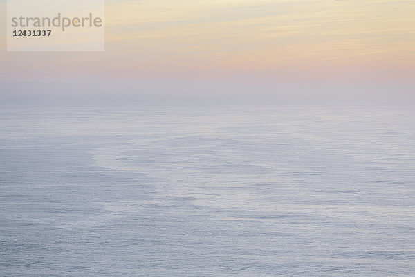 Der offene Ozean  die Wasseroberfläche ruhig und grau und der Schein der Sonne in der Morgendämmerung am Horizont.