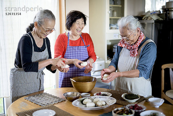 Drei ältere Frauen stehen um einen Tisch in einer Küche und machen Sushi.