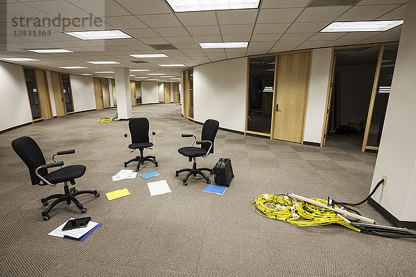 Drei Stühle  die allein in einem offenen Bereich in einem unbesetzten Büroraum sitzen.