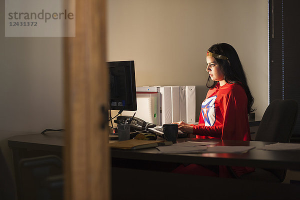 Eine hispanische Geschäftsfrau als Superheldin an ihrem Bürocomputer