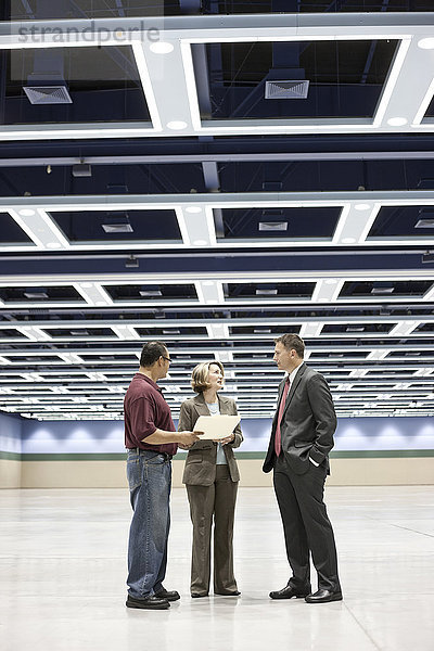 Drei Planer von Geschäftstreffen sprechen auf dem Boden eines Kongresszentrums.