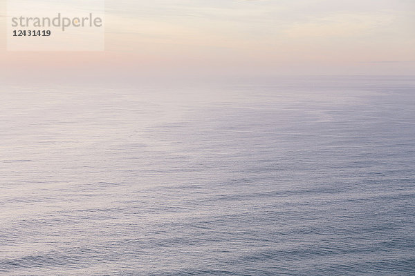 Der offene Ozean  die Wasseroberfläche ruhig und grau und der Schein der Sonne in der Morgendämmerung am Horizont.