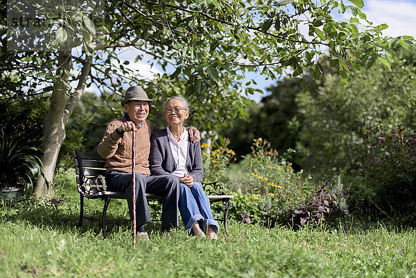 Ehemann und Ehefrau  älterer Mann mit Hut und Frau sitzen nebeneinander auf einer Bank in einem Garten.