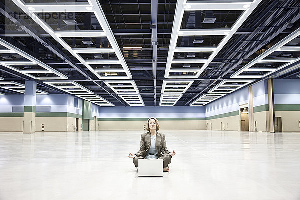 Eine Geschäftsfrau in einer Yoga-Pose mit einem Laptop-Computer in der Mitte einer Kongresszentrum-Arena.