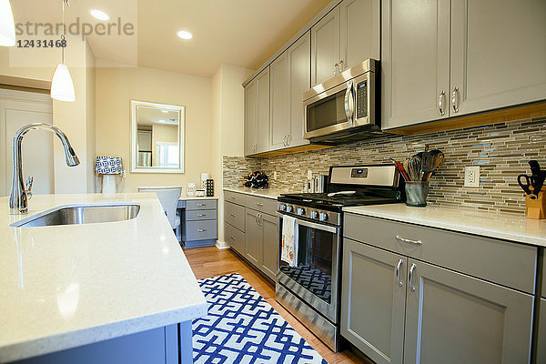 Moderne Wohnküche mit grün-grauen Einbauschränken  einer Kücheninsel und blauem Teppichboden.