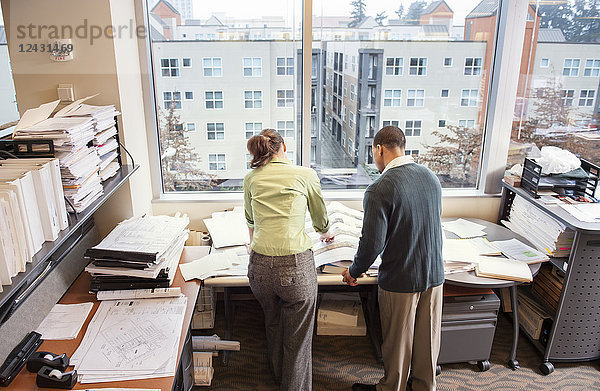 Ein Blick von hinten auf zwei Personen  die die Pläne für einen neuen Raum in ihrem Büro durchgehen.