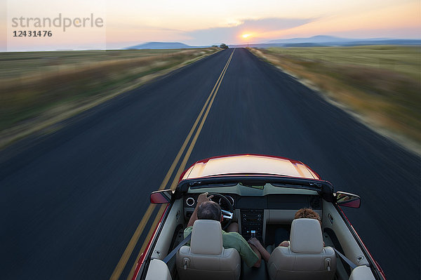 Blick von hinten auf ein älteres Ehepaar in einem Cabrio-Sportwagen  das bei Sonnenuntergang im Osten des Staates Washington  USA  auf einer Autobahn fährt.